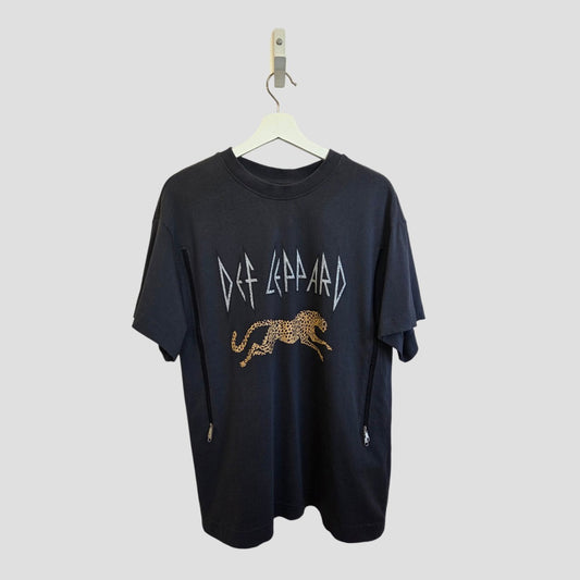 An upcycled H&M Def Leppard band T-shirt (nursing & pumping, size M) with a leopard print and stylized white band lettering hangs on a white hanger against a plain gray background.