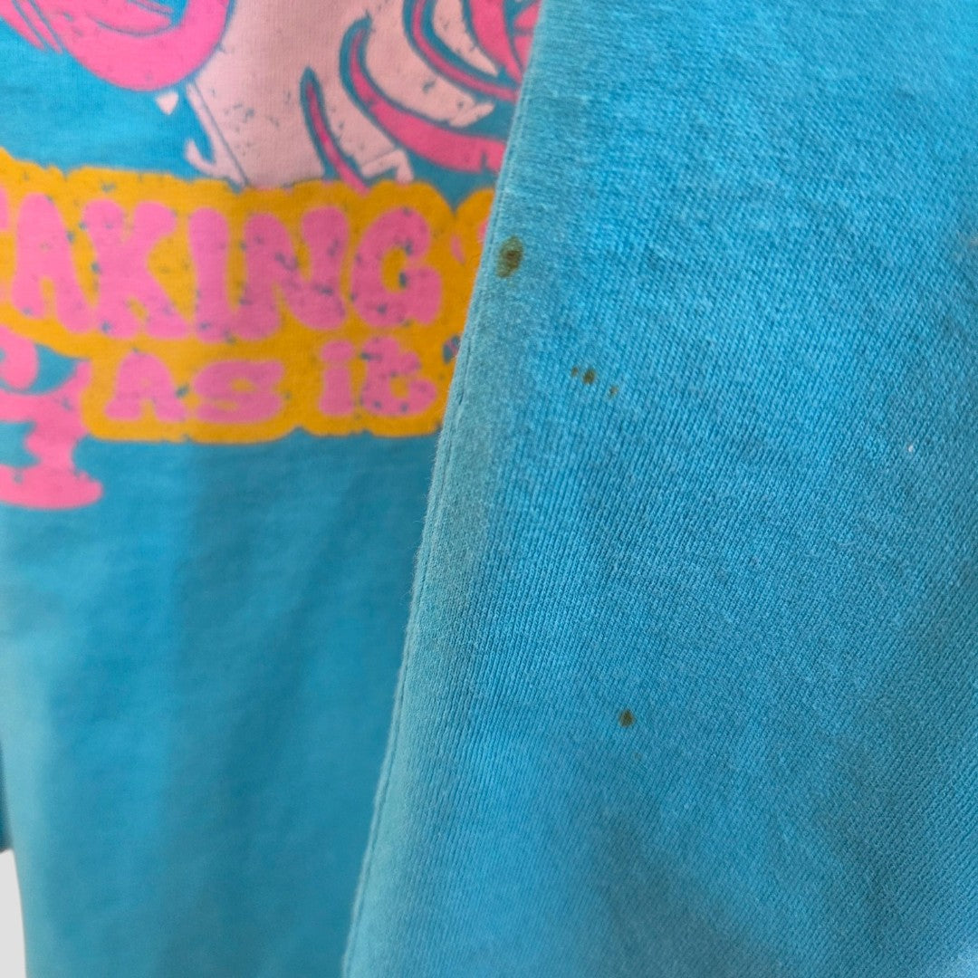 Close-up of an Upcycled Breastfeeding & Pumping Turquoise/Pink Girl t-shirt (L, UK14/16) by Primark, showing small dark stains and part of a pink/yellow graphic—highlighting its casual, affordable nursing style.