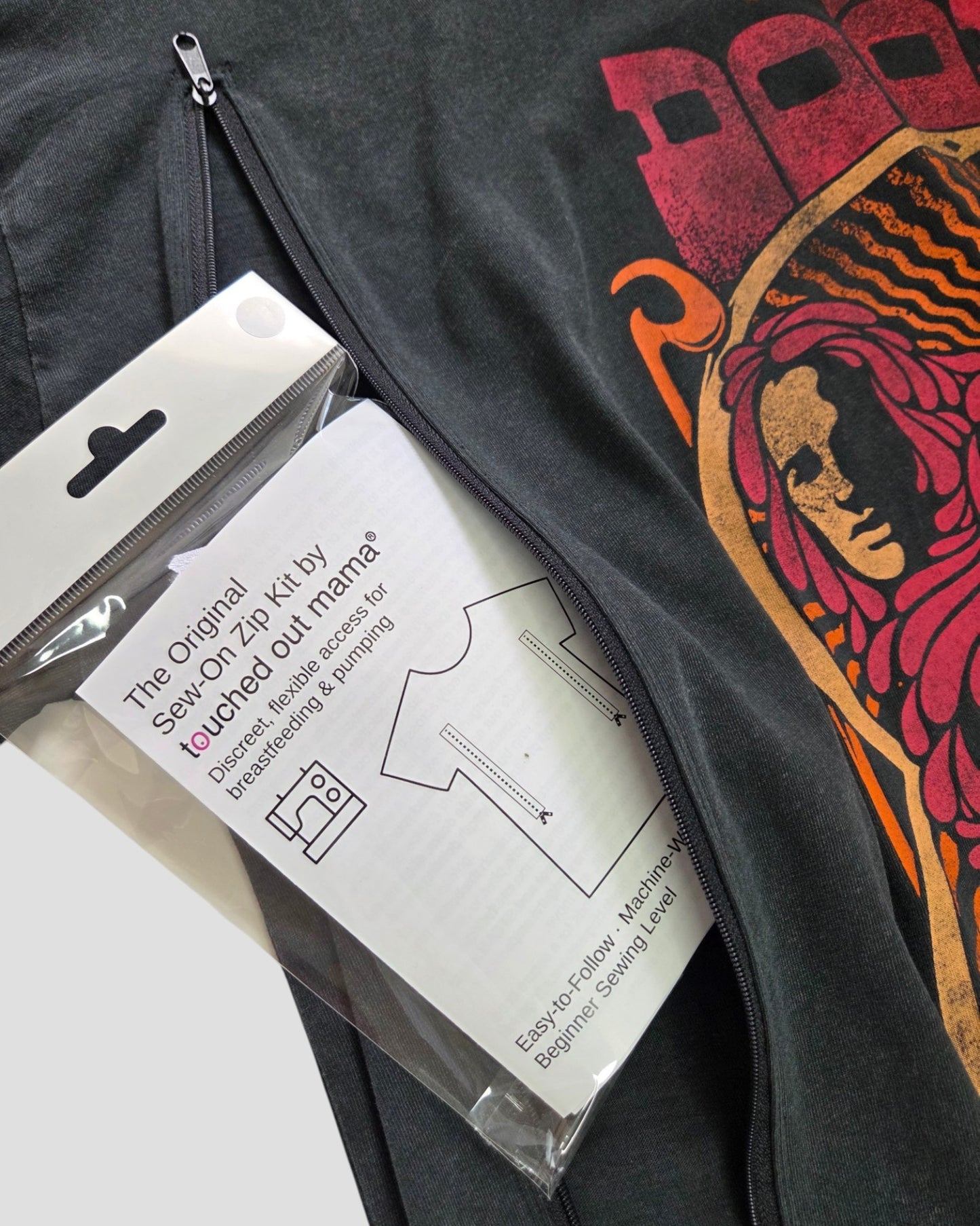 The Original Sew-On Zip Kit for Breastfeeding & Pumping Access by touched out mama peeks through a black shirt with a colorful abstract face, inspiring you to upcycle tees or craft DIY nursing tops using handy sewing symbols.