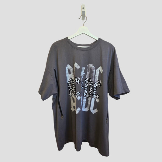 The AC/DC Upcycled Breastfeeding & Pumping Grey Leopard Band T-shirt XL (100545) is a loose-fit, eco-friendly option with bold silver geometric lettering and leopard accents, shown hanging on a white hanger against a light background.