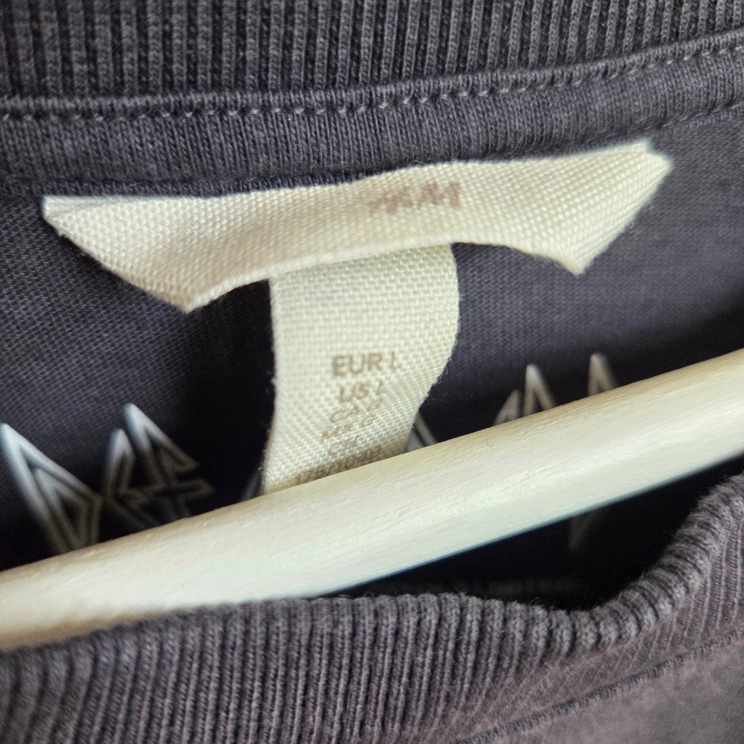 Close-up of an H&M Upcycled Breastfeeding & Pumping Grey Def Leppard Band t-shirt (L, 100579) tag on a dark garment, with part of a white hanger underneath—an eco-friendly, affordable choice for stylish nursing wear.