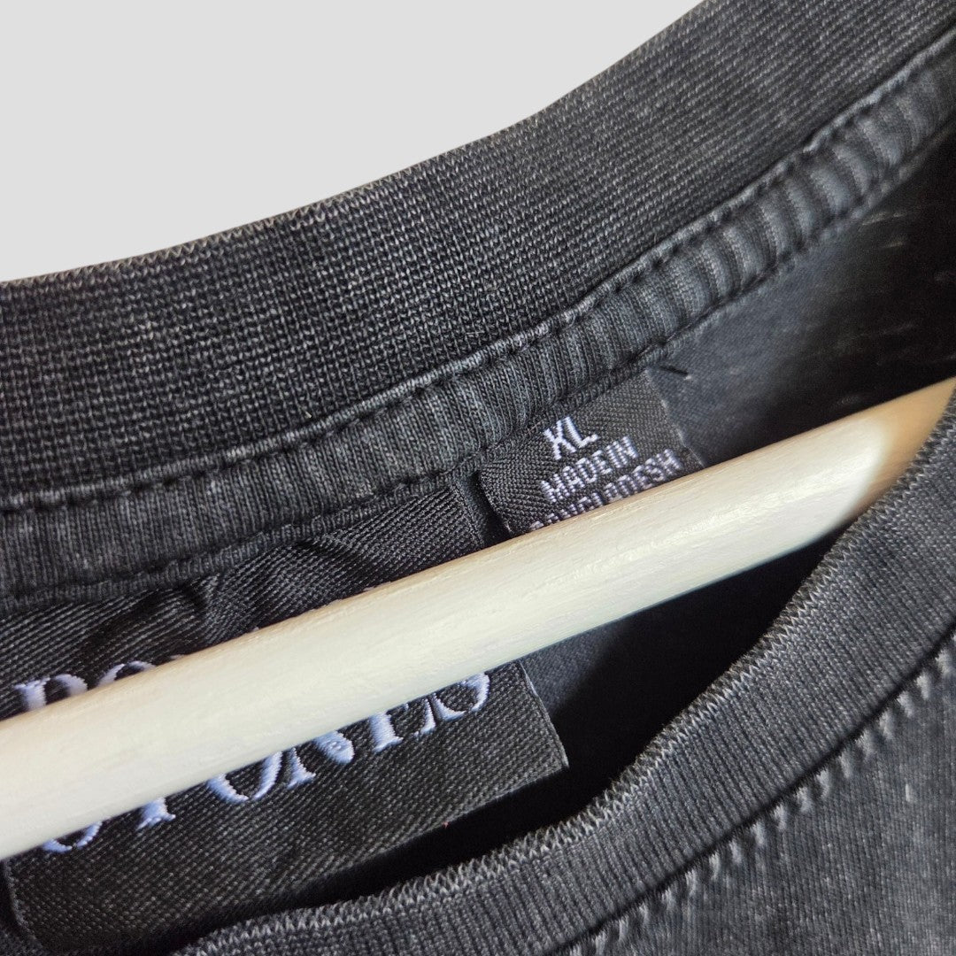 Close-up of a Primark Upcycled Breastfeeding & Pumping Black The Rolling Stones Voodoo Band t-shirt (XL, 100566) on a hanger, showing the collar, stitching, and label that reads XL MADE IN BANGLADESH.