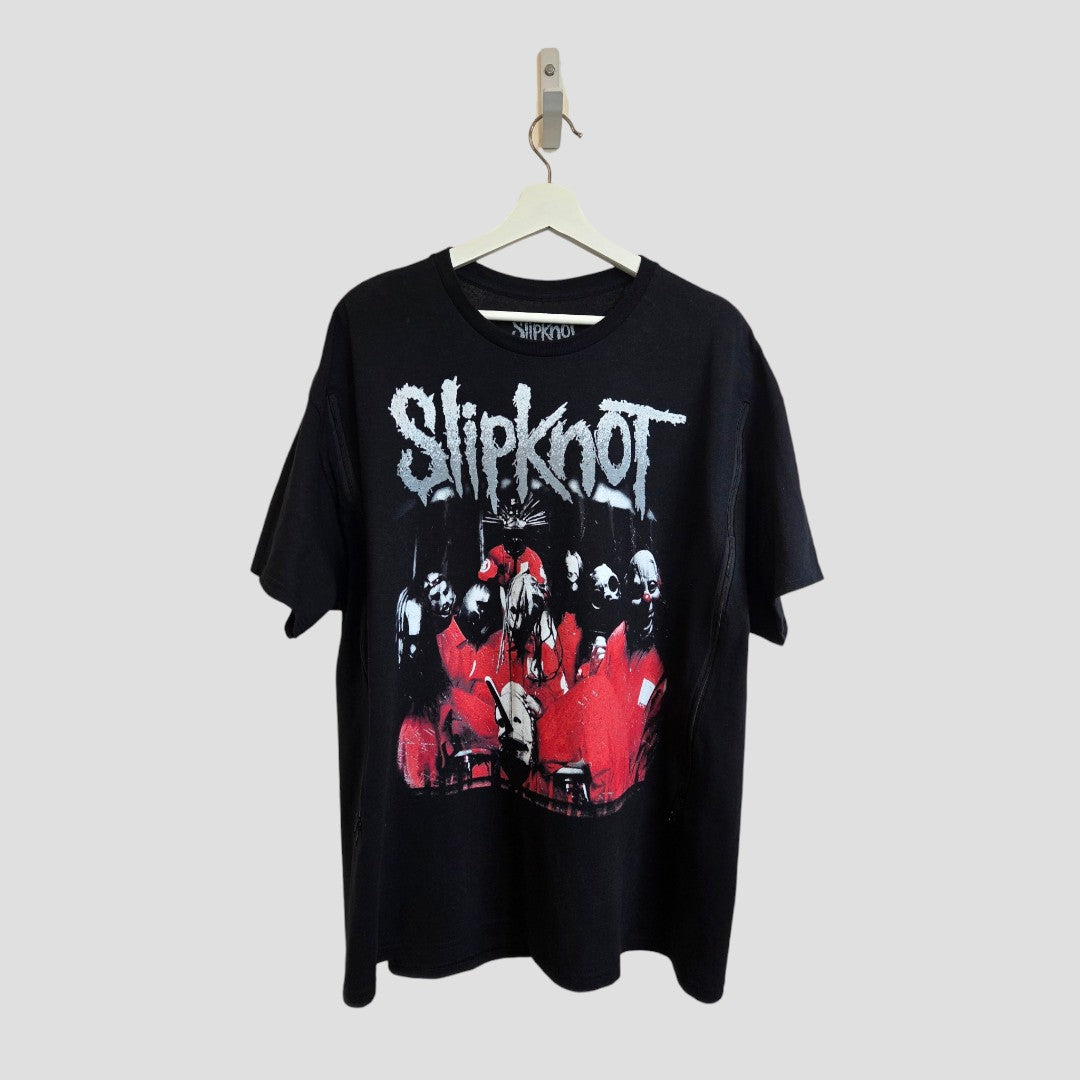 An upcycled Slipknot band t-shirt (XL) for breastfeeding and pumping hangs on a white hanger. Black with bold gray letters and a red/white graphic of masked members, it features eco-friendly fabric. Background is light gray. Brand: Slipknot.