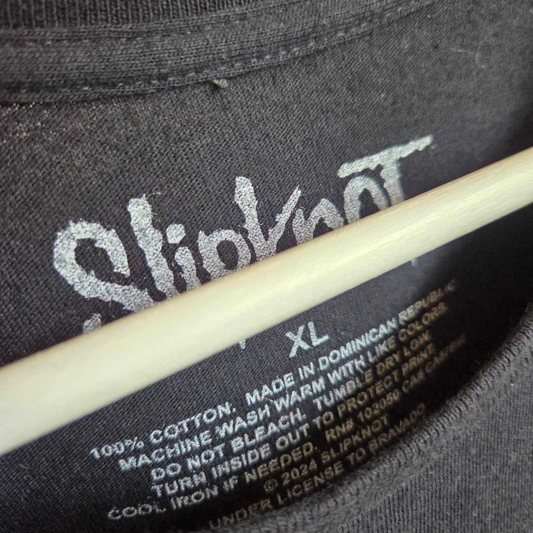Close-up of an upcycled Slipknot black/red band t-shirt (XL, 100584), showing inner neck label with logo, size, and care instructions. A light rod partially obstructs the view—a bold eco-friendly nursing & pumping clothing option.