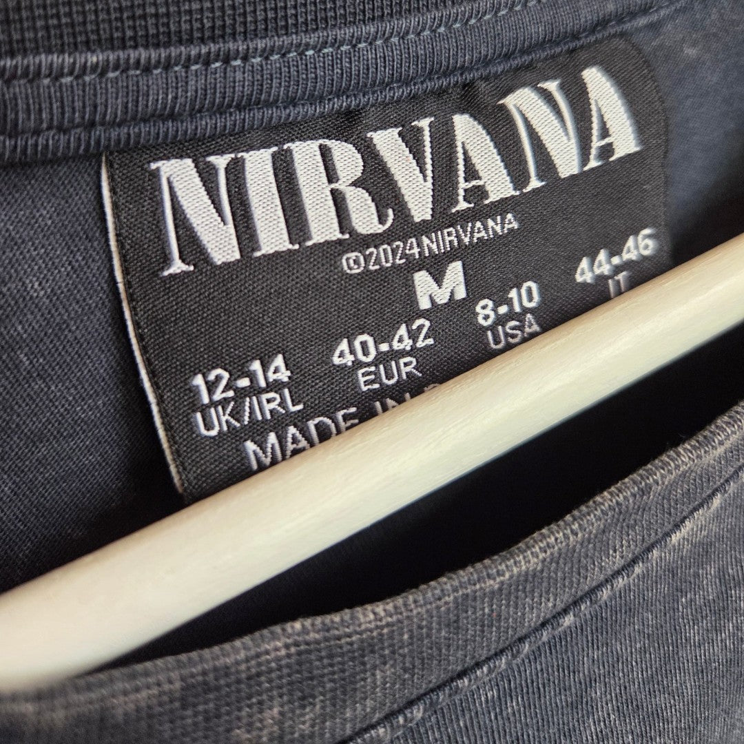 Close-up of a black clothing label inside a Primark Upcycled Breastfeeding & Pumping Grey/Turquoise Nirvana Angel Band t-shirt (M, UK12/14), copyright ©2024, on a hanger—perfect for stylish, affordable maternity wear fans.