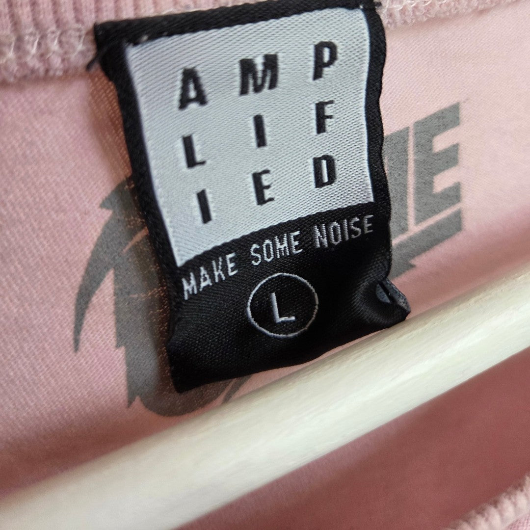 A close-up of a black and white Amplified label on pink fabric reading "AMPLIFIED" and "MAKE SOME NOISE" shows the eco-friendly Upcycled Breastfeeding & Pumping Pink David Bowie Band t-shirt (L, 100531), designed for comfort and style.
