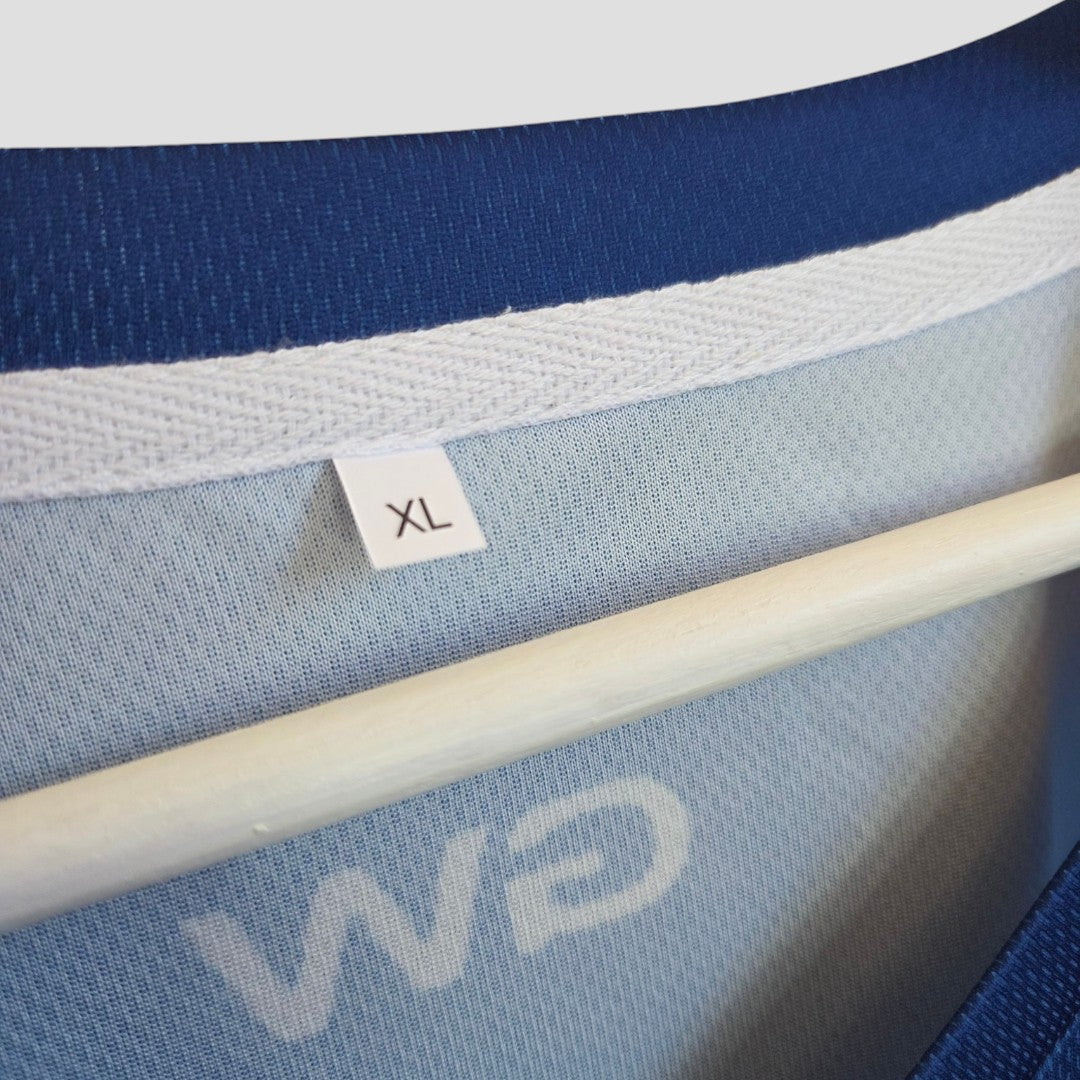 Close-up of an affordable Amazon Upcycled Breastfeeding & Pumping Blue Off Campus Garrett Graham Ice Hockey Jersey t-shirt XL (100589) on a hanger, showing the white XL size tag, interior fabric, and partial reversed logo—ideal for nursing.