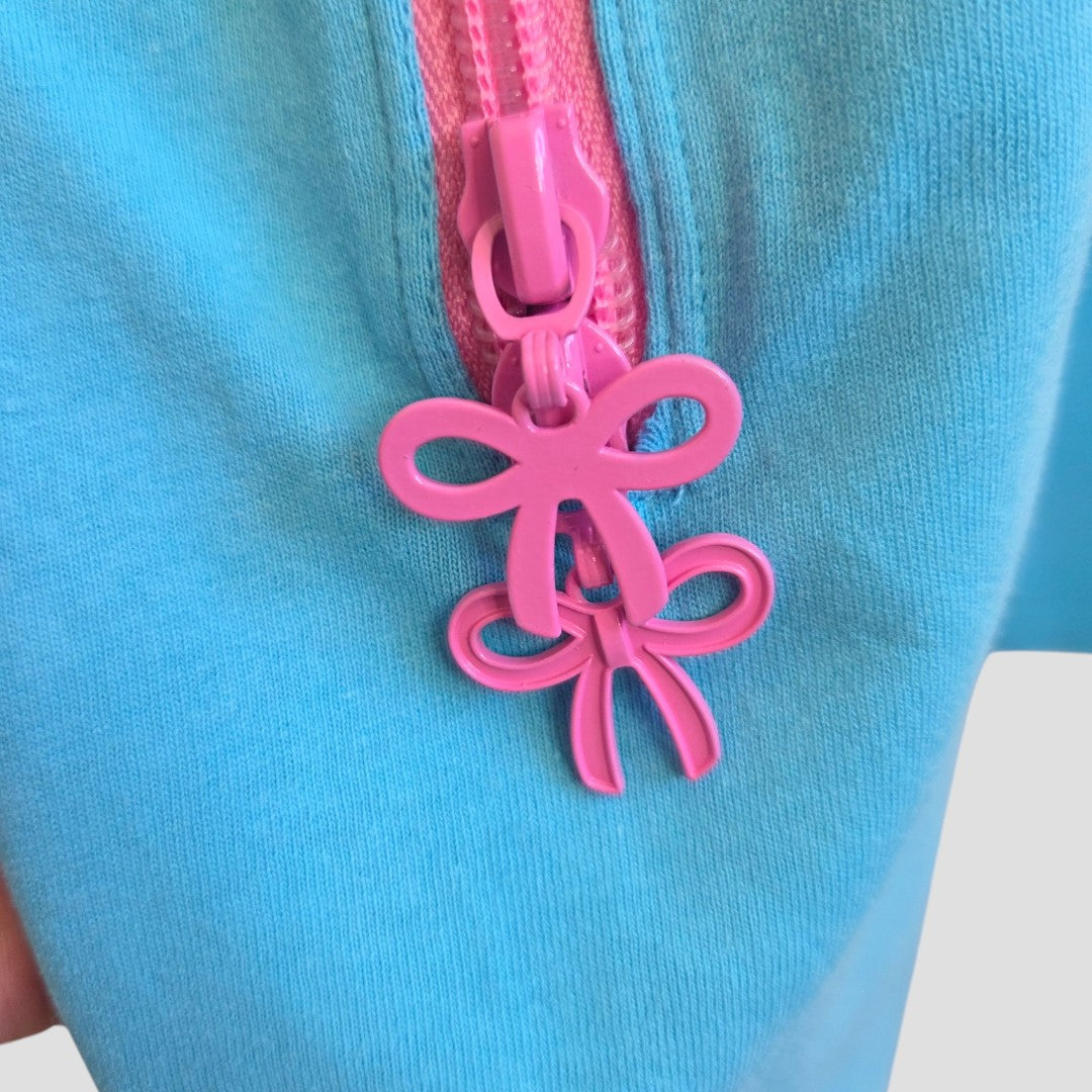 Close-up of the Upcycled Breastfeeding (Nursing) & Pumping Turquoise/Pink Girl t-shirt XL (UK18/20) by Primark, featuring blue fabric with a pink zipper. The bow-shaped zipper pull adds a stylish touch, making this affordable nursing top both functional and fashionable.