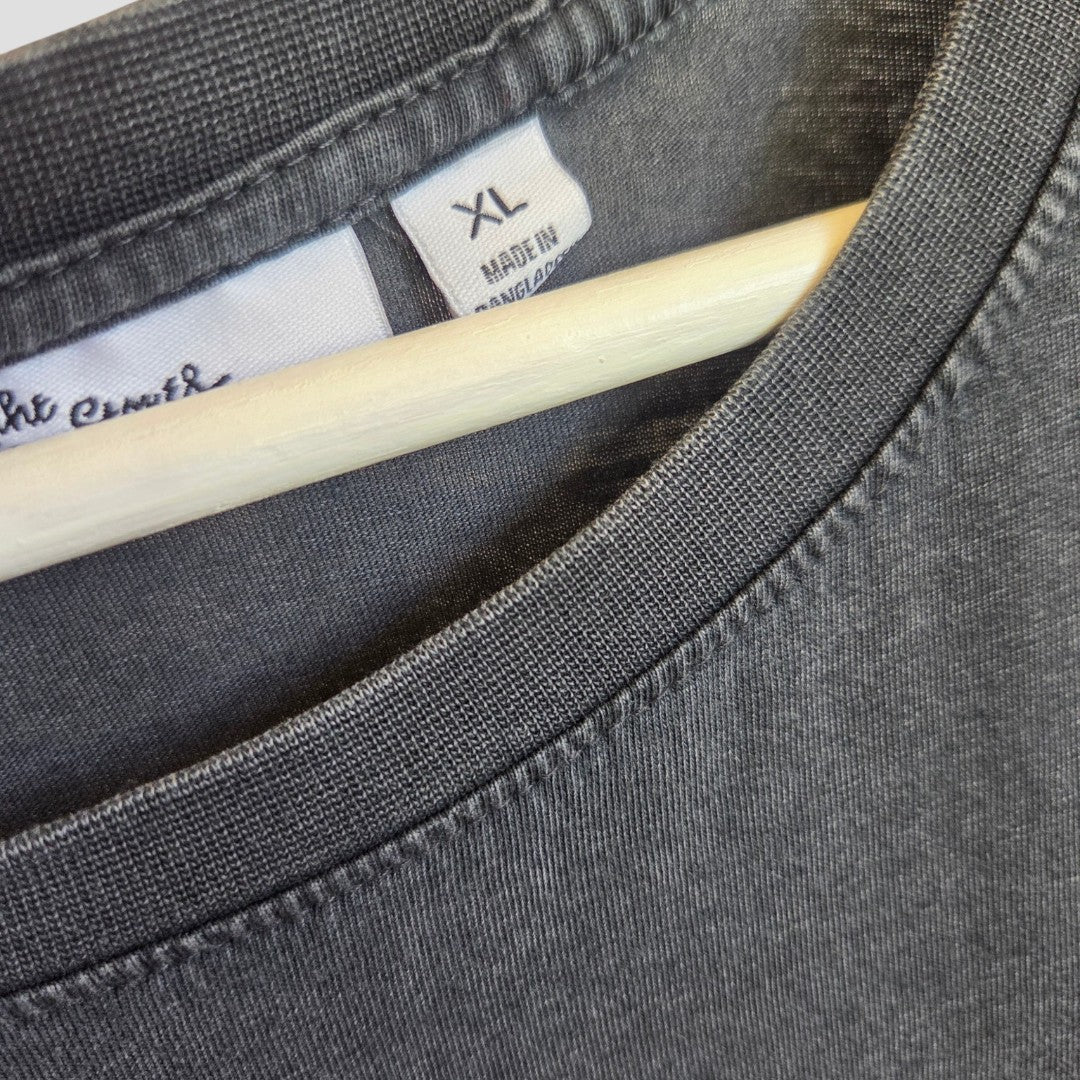 Close-up of a Next Upcycled Breastfeeding (Nursing) & Pumping Grey Floral The Rolling Stones Band t-shirt in size XL (100557) on a wooden hanger, highlighting the stitching details near the collar and a MADE IN BANGLADESH tag. This comfortable piece is thoughtfully designed as an eco-friendly alternative for modern parents, combining style and function.