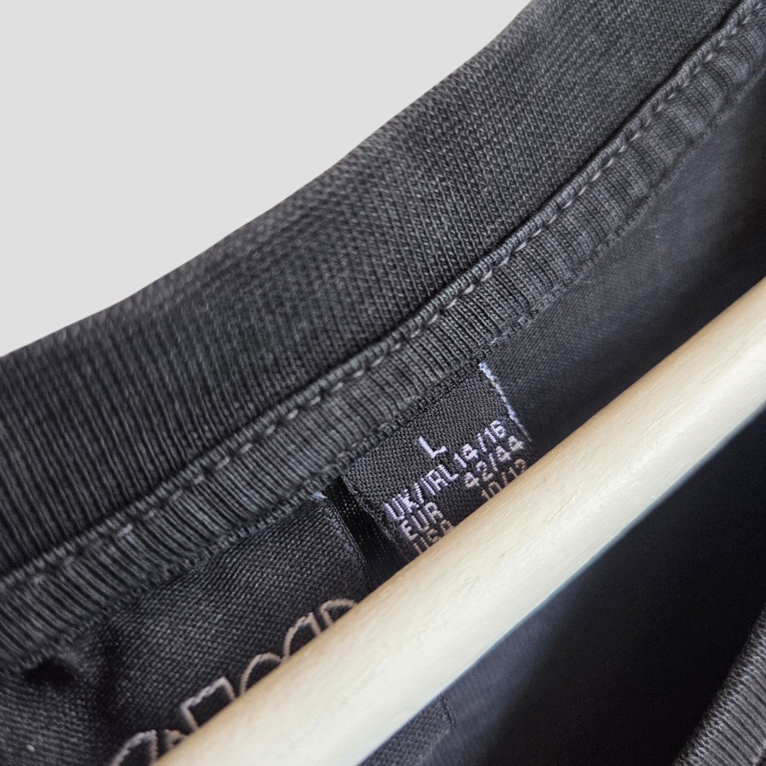 Close-up of an Upcycled Breastfeeding (Nursing) & Pumping The Doors Oversized Band t-shirt dress in black, size L (UK14/16), by Primark, displayed on a wooden hanger with a visible Primark label featuring multilingual information.