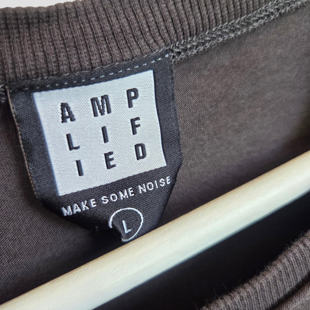 A black and white clothing label reading "AMPLIFIED" and "MAKE SOME NOISE" above the size L is sewn into a dark, eco-friendly Upcycled Breastfeeding & Pumping Black/Pink Metallica Band t-shirt (size L, by Amplified), displayed on a hanger.