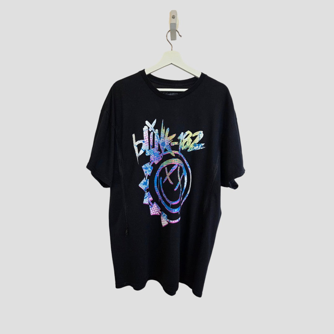 An Upcycled Breastfeeding (Nursing) & Pumping Black Colourful Blink-182 Smile Band t-shirt XXL (100615) by Blink-182, crafted from 100% cotton and showcasing a vibrant, pixelated band logo with a smiley face graphic, is displayed on a white hanger against a plain gray background.