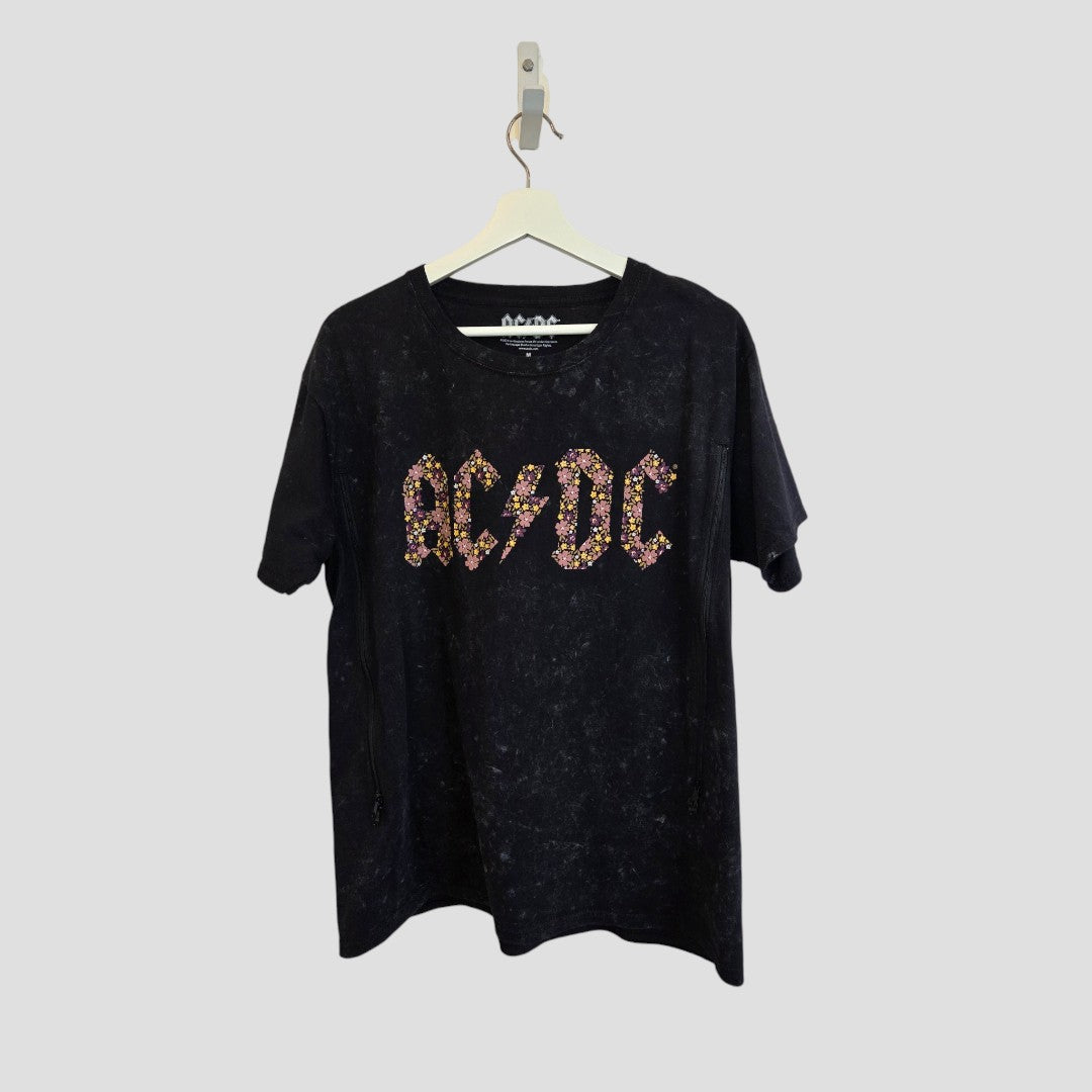 Upcycled breastfeeding (nursing) and pumping black floral AC/DC band t-shirt (size M) by AC/DC, featuring studded, colorful lettering across the chest—an eco-friendly, affordable wardrobe essential that adds rock style to motherhood essentials. Displayed on a white hanger against a plain light gray background.