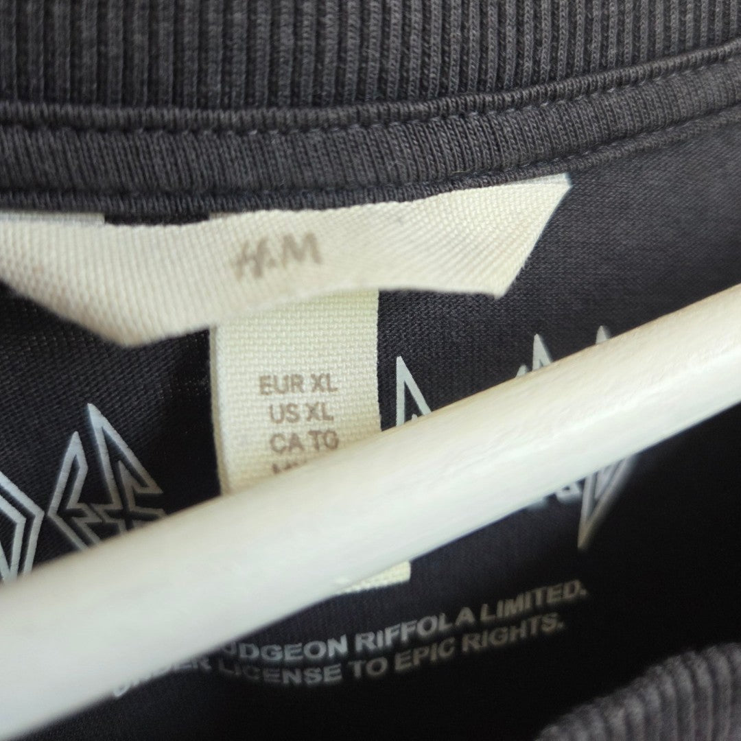 Close-up of a black H&M Upcycled Breastfeeding (Nursing) & Pumping Grey Def Leppard Band t-shirt’s collar and tags in size XL (EUR XL, US XL, CA XL), with part of a white print and a wooden hanger visible—an affordable maternity wear option for everyday comfort.