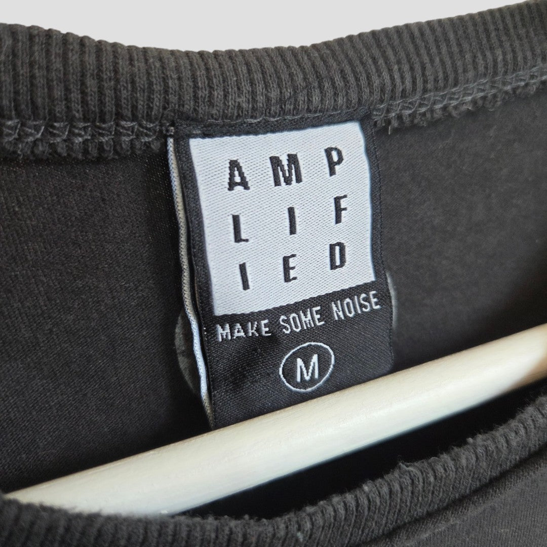 A close-up of the tag on the Upcycled Breastfeeding (Nursing) & Pumping The Beatles Colourblock Band t-shirt (size M) by Amplified shows “AMPLIFIED” and “MAKE SOME NOISE” printed on it. Crafted with eco-friendly materials, this black shirt is displayed on a light wooden hanger.