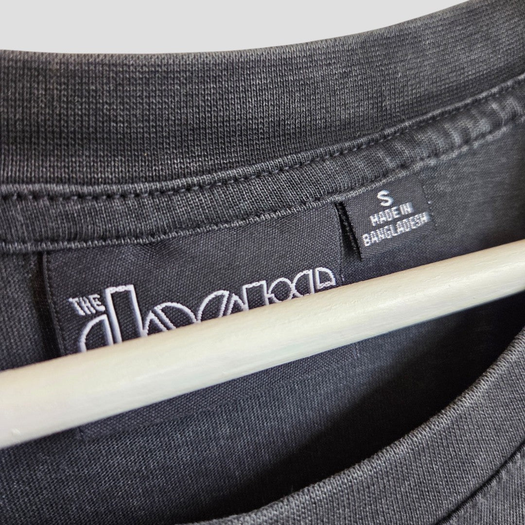 Close-up of a black Primark Upcycled Breastfeeding (Nursing) & Pumping The Doors Strange Days Oversized Band t-shirt, size S, with a tag reading “Made in Bangladesh.” A clothing hanger peeks out beneath the collar, emphasizing this eco-friendly and affordable choice—perfect for those seeking stylish, sustainable options.