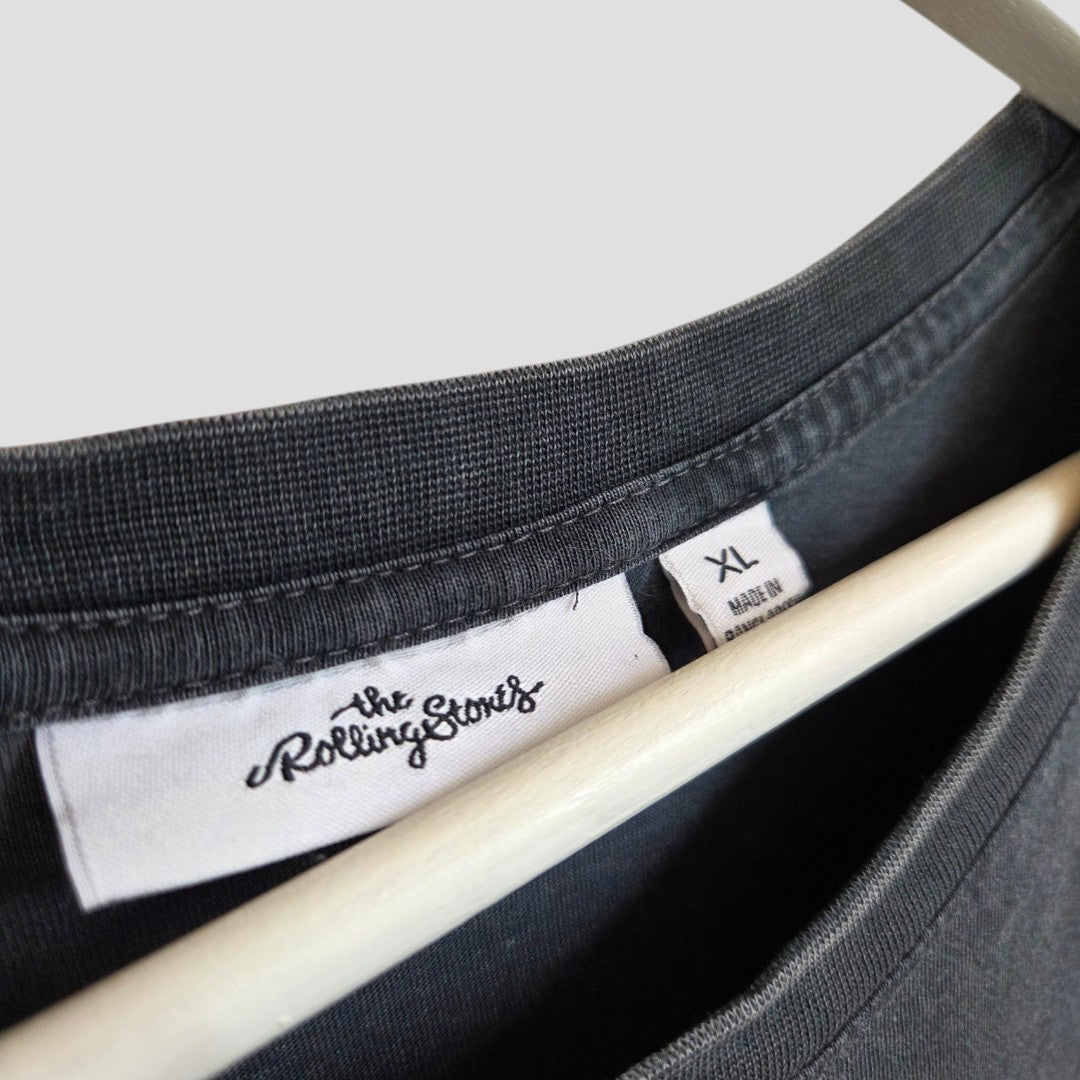Close-up of a grey Upcycled Breastfeeding (Nursing) & Pumping The Rolling Stones Eagle Band T-shirt by Next in size XL, displayed on a hanger with two visible tags near the collar—one featuring The Rolling Stones branding and the other indicating XL size and made in Bangladesh. This affordable piece easily complements your everyday style, perfect for building a casual wardrobe or pairing seamlessly with nursing clothing essentials.