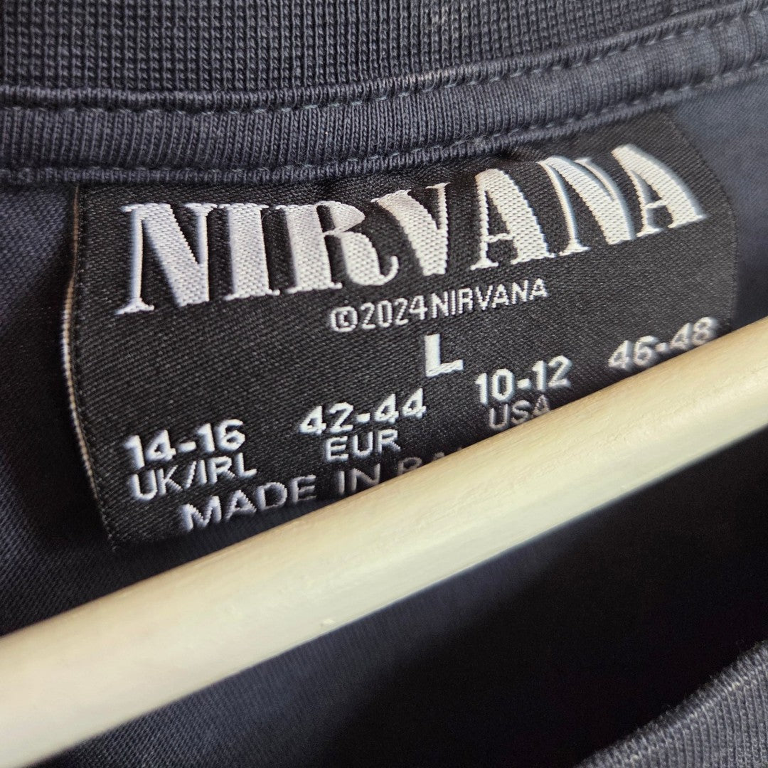 Close-up of a black clothing tag inside a turquoise nursing and pumping t-shirt, featuring the Primark brand, product name “Nirvana Turquoise Angel,” size L (UK14/16), 2024 copyright, and multiple international size conversions in white text. A hanger is partially visible at the bottom.