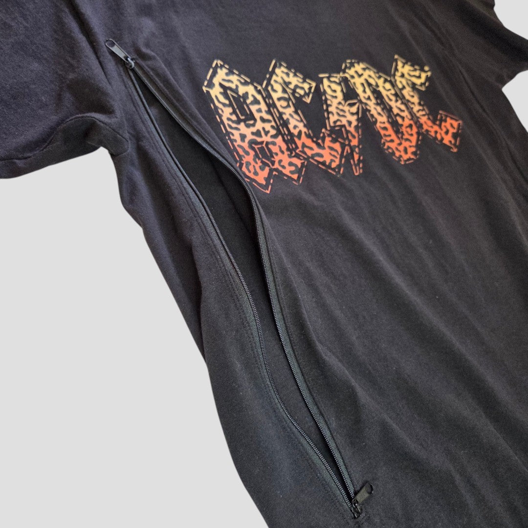 Upcycled Breastfeeding (Nursing) & Pumping Black Leopard AC/DC Band t-shirt (size M) by AC/DC, featuring a bold orange-yellow graphic text on black fabric and a large diagonal zipper from the side to the bottom for convenient breastfeeding access, displayed on a light gray background.