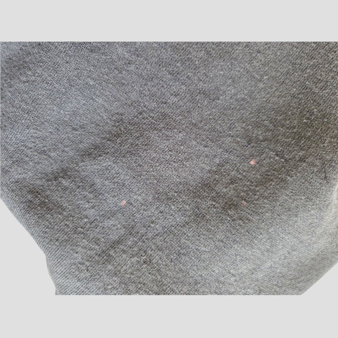A close-up of the gray fabric from the H&M Upcycled Breastfeeding (Nursing) & Pumping Grey Pink Floyd Band sweatshirt dress (size L, 100548), showing two small pinkish spots and a slightly worn texture that may indicate minor wear or damage.