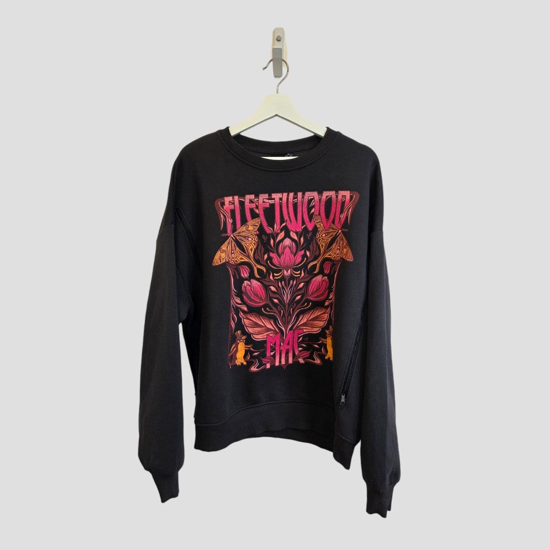 A black upcycled breastfeeding and pumping sweatshirt from Primark hangs on a hanger, featuring a bold, colorful graphic with the text “Fleetwood Mac” on the front in pink, red, and orange psychedelic floral tones. Blending style with comfort for everyday wear, this UK12/14 (M) band sweatshirt is inspired by trendy finds and designed for both nursing and pumping moms.