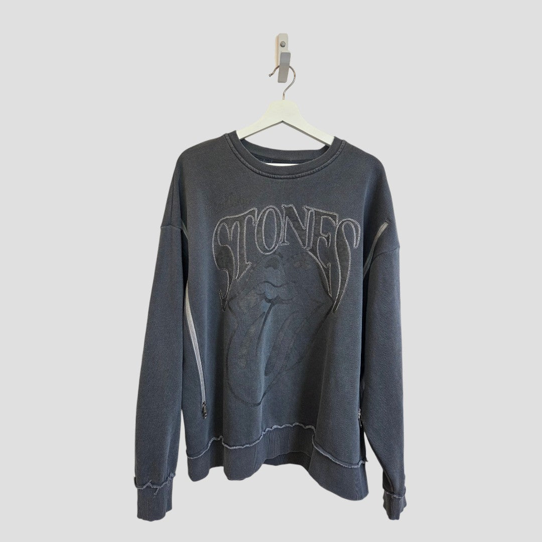 An affordable and stylish choice, the Primark Upcycled Breastfeeding (Nursing) & Pumping Grey Embroidered The Rolling Stones Band Sweatshirt (size M, 100570) features a dark gray crewneck design with “STONES” lettering and a large tongue and lips graphic on the front, shown hanging on a white hanger against a light gray background.
