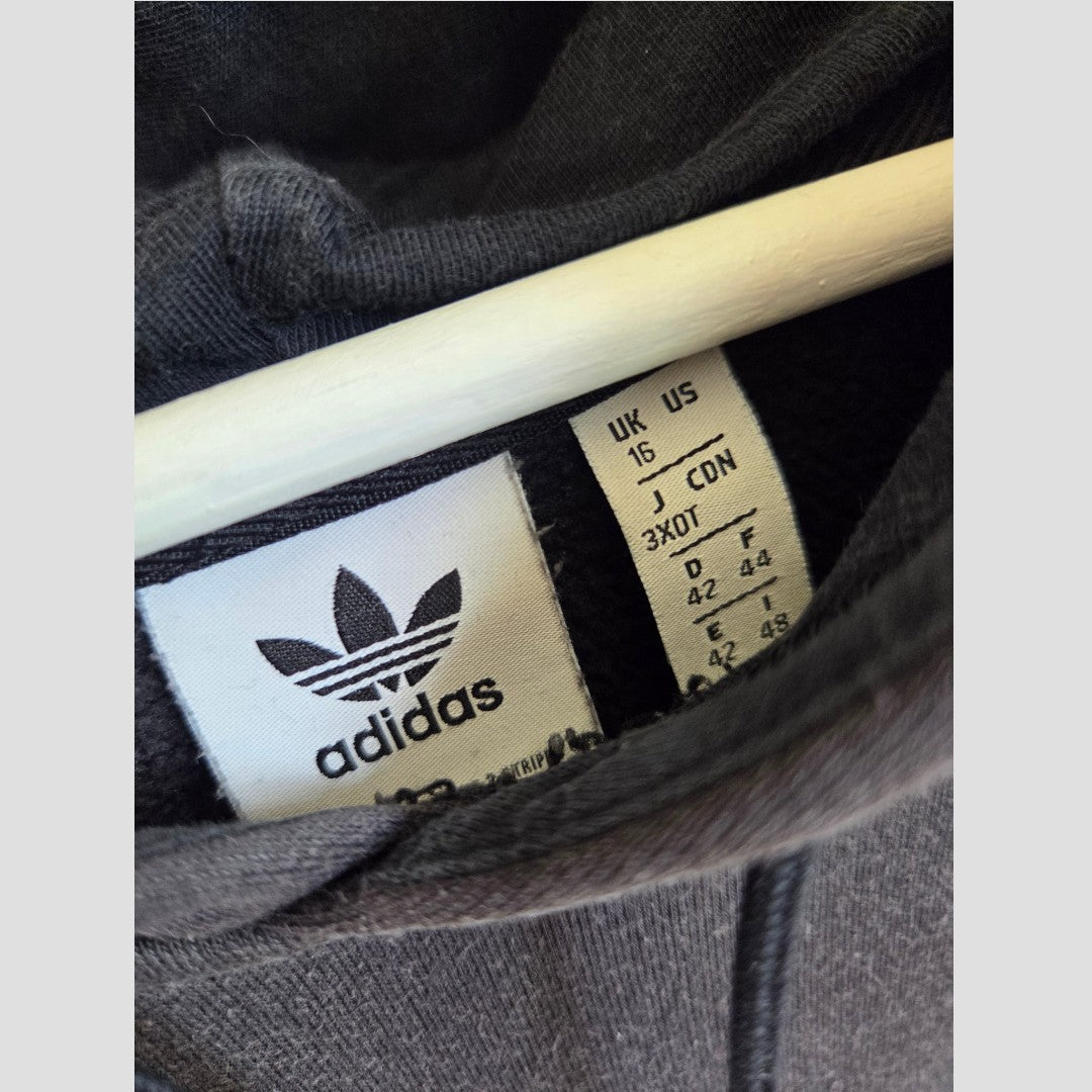 Close-up of a black Adidas garment label from the Upcycled Breastfeeding (Nursing) & Pumping Black Adidas White Logo Hoodie UK16 (100486), showing size information: UK 15, US 16, J 3XO, D 42, E 44. The iconic Adidas logo and trefoil appear above the sizing details, reflecting the brand’s commitment to quality—features equally valued in upcycled eco nursing clothing and affordable nursing wear.