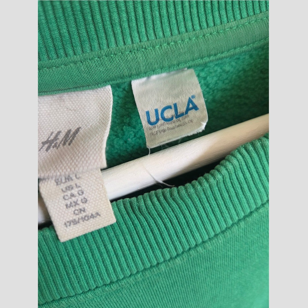 Close-up of green Upcycled Breastfeeding (Nursing) & Pumping UCLA sweatshirt collars on a hanger, featuring two clothing tags: an H&M tag with size details and a white tag with blue UCLA text—a stylish and eco-friendly choice for your everyday wardrobe.