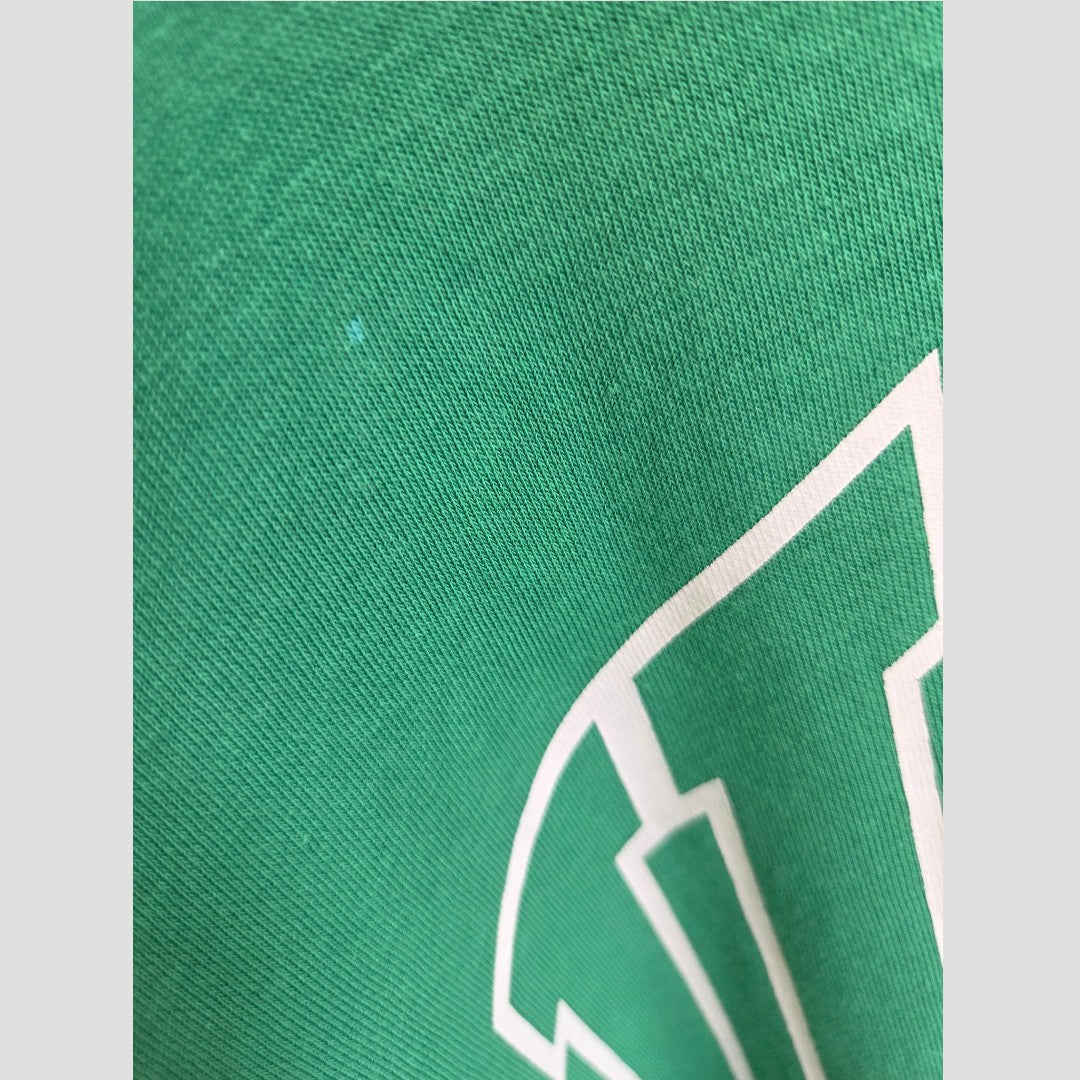 Close-up of green fabric from the Upcycled Breastfeeding (Nursing) & Pumping Green UCLA sweatshirt L (100629) by H&M, featuring a partial white geometric design on the lower right side. The texture of this eco-friendly, affordable nursing clothing is visible.