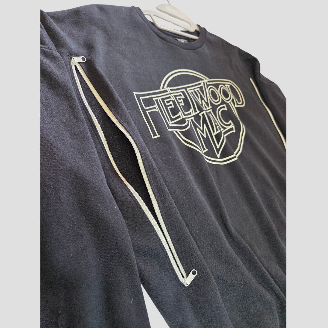 The George Upcycled Breastfeeding (Nursing) & Pumping Black/White Fleetwood Mac Band Sweatshirt (size M, 100576) features bold white lettering on the front and a discreet diagonal zippered opening along the sleeve for easy nursing or pumping access. Stylish and affordable, this breastfeeding-friendly top is pictured hanging on a white hanger against a plain light background.