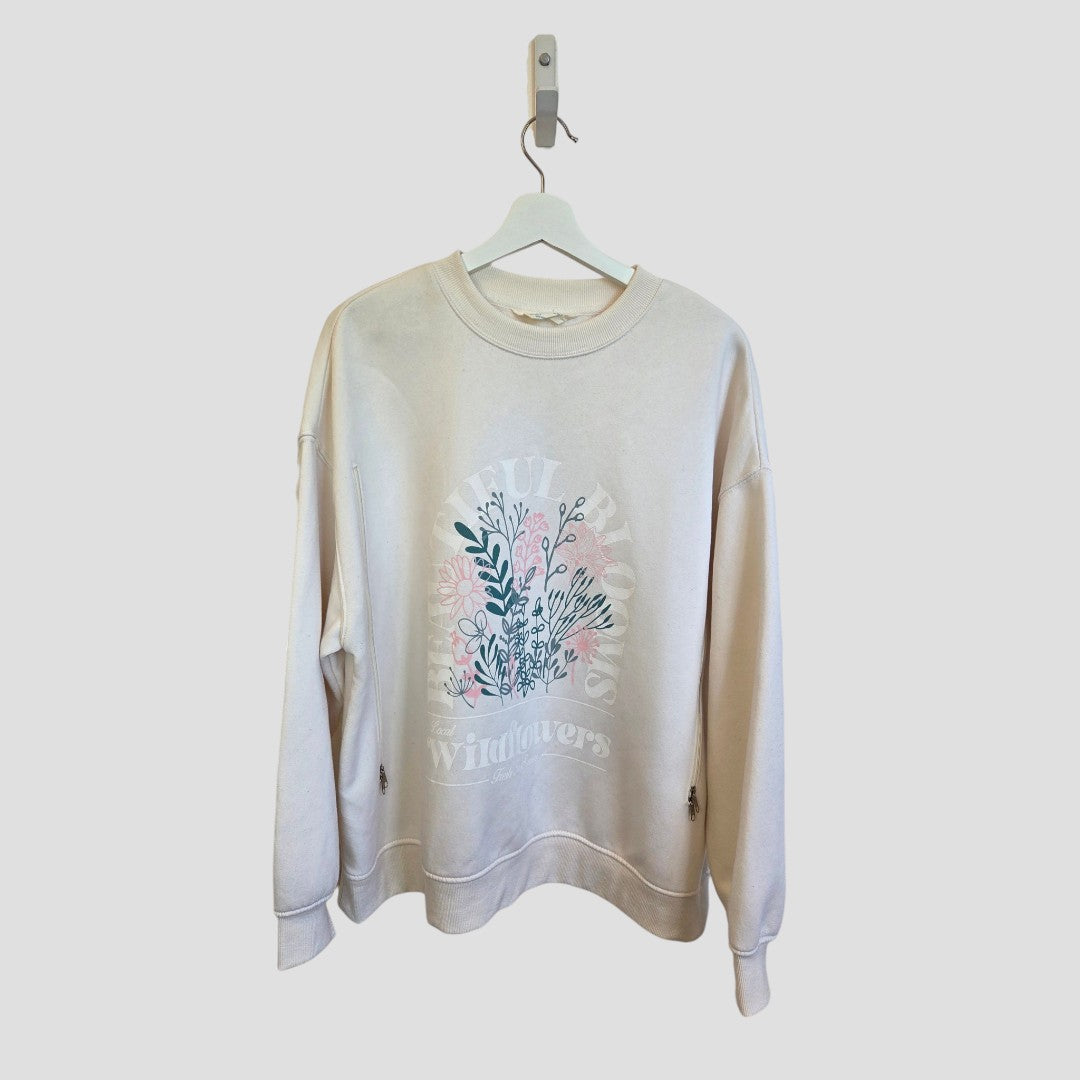 An Upcycled Breastfeeding (Nursing) & Pumping Cream Wildflowers sweatshirt (XL, 100645) from Primark, featuring a floral graphic and the words “Wildflowers,” designed for comfort during nursing, hangs on a white hanger against a light gray background.