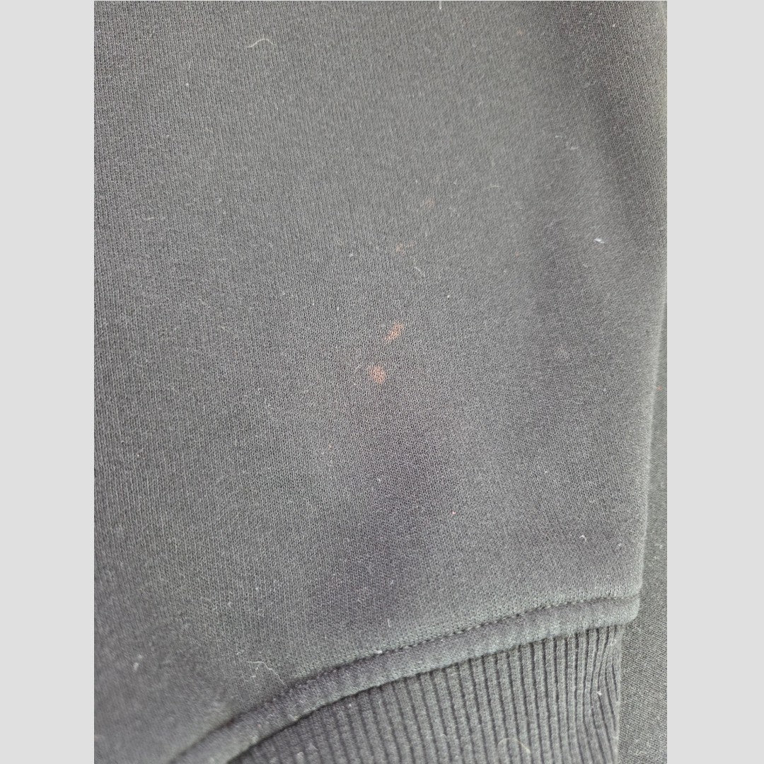Close-up of the black fabric on the Primark Upcycled Breastfeeding (Nursing) & Pumping Black Basquiat Graphic hoodie XL (UK18/20) (100633), possibly part of a sleeve or cuff, showing a small, faint reddish stain and some visible lint or dust particles.