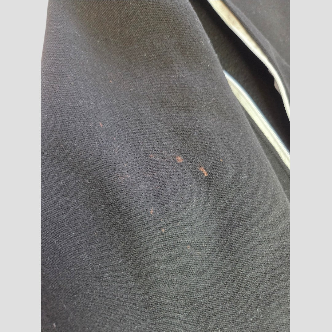 A close-up of the Primark Upcycled Breastfeeding (Nursing) & Pumping Black Basquiat Graphic hoodie XL (UK18/20) fabric, featuring several small reddish-brown stains and a partially visible zipper on the right side.