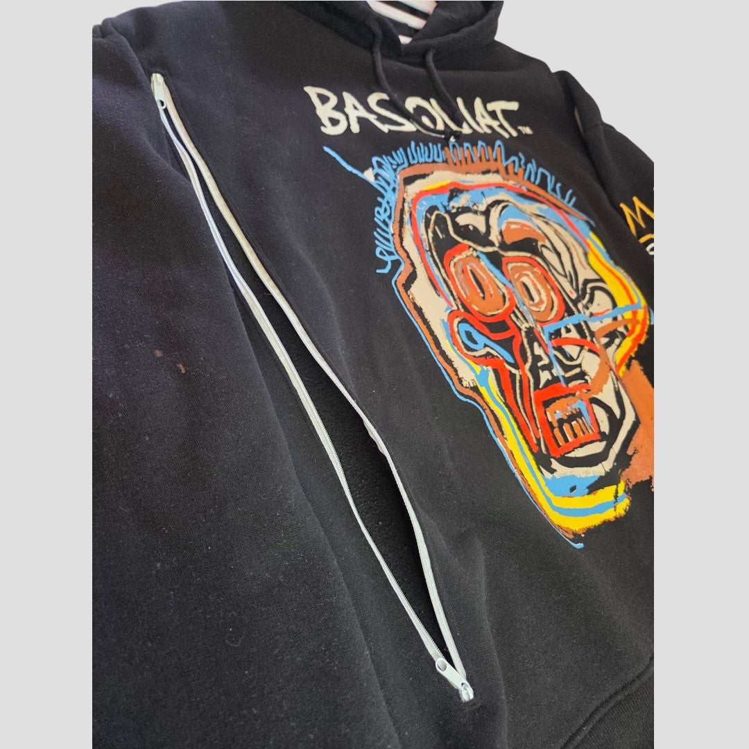 Introducing the Upcycled Breastfeeding (Nursing) & Pumping Black Basquiat Graphic Hoodie XL (UK18/20) (100633) by Primark—a striking black hoodie featuring colorful abstract face art, a visible white zipper running diagonally, and the word BASQUIAT partially displayed on the chest. This eco-friendly piece combines bold style with practical functionality, making it a unique and expressive fashion choice for those seeking sustainable alternatives.
