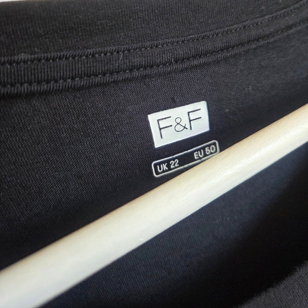 Close-up of a black garment label featuring the F&F brand and size details: UK 22, EU 50. A wooden hanger appears beneath the tag. This upcycled Breastfeeding & Pumping Black Christmas Candy Canes t-shirt (UK22, product code 100657) is an excellent affordable choice for comfortable nursing wear.