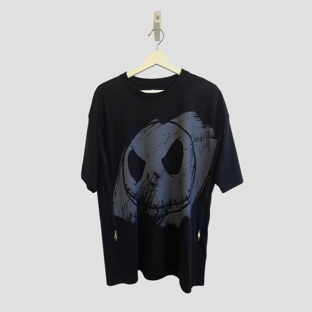 A black Upcycled Breastfeeding (Nursing) & Pumping Nightmare Before Christmas Oversized t-shirt by Primark, size S (UK10/12), featuring a large abstract gray sinister smiley face graphic, is displayed on a wooden hanger against a plain light gray background.