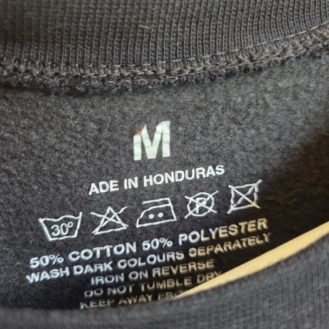 A black clothing label for the Upcycled Breastfeeding (Nursing) & Pumping Black Here for the Boos sweatshirt M (100652) displays size M, MADE IN HONDURAS, material composition of 50% cotton and 50% polyester, along with care instructions featuring laundry symbols and text—including guidance on washing, ironing, and tumble drying—making it a practical and affordable choice for nursing or breastfeeding apparel.