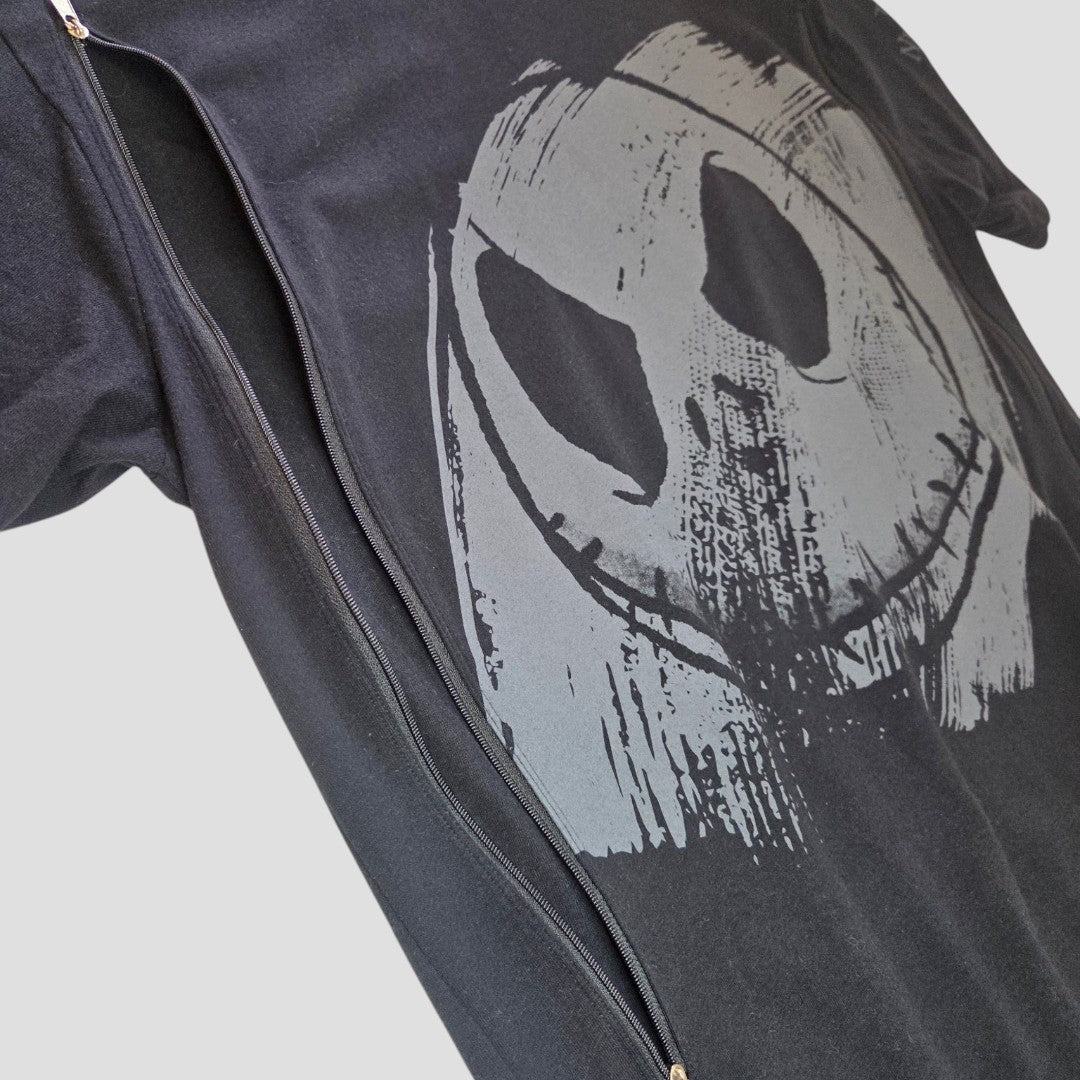 A black “Nightmare Before Christmas” oversized t-shirt by Primark, featuring a large, gray, distressed smiley face design and worn partially unzipped under a black jacket against a light gray background—this upcycled S (UK10/12) nursing and pumping tee combines comfort with style, making it an affordable and practical choice for breastfeeding moms.