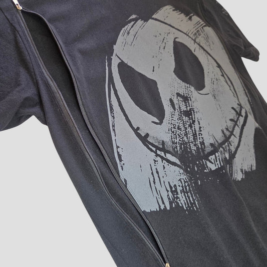 A black “Nightmare Before Christmas” oversized t-shirt by Primark, featuring a large, gray, distressed smiley face design and worn partially unzipped under a black jacket against a light gray background—this upcycled S (UK10/12) nursing and pumping tee combines comfort with style, making it an affordable and practical choice for breastfeeding moms.