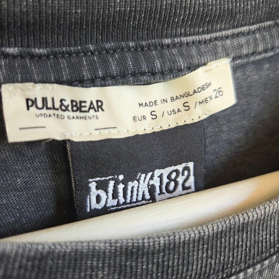 Clothing tags on the inside of the Upcycled Breastfeeding (Nursing) & Pumping Grey Blink-182 Flower Oversized Band t-shirt S (100620) collar, showing Pull&Bear brand and size information above a Blink-182 logo tag.