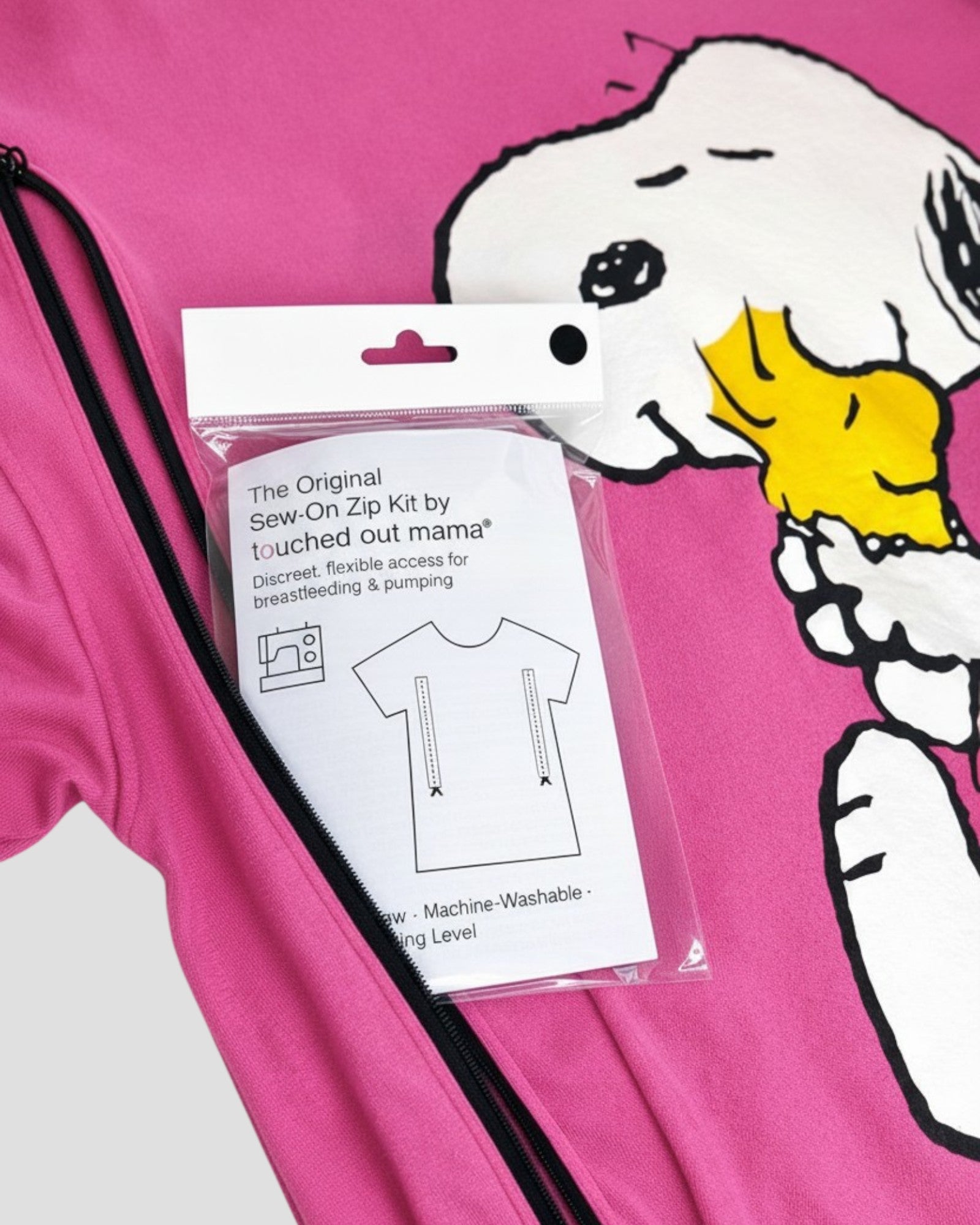 A pink nursing top with a large Snoopy graphic, partially unzipped, displays The Original Sew-On Zip Kit for Breastfeeding & Pumping Access by touched out mama—a DIY kit for discreetly adding zip access to t-shirts for nursing and pumping.